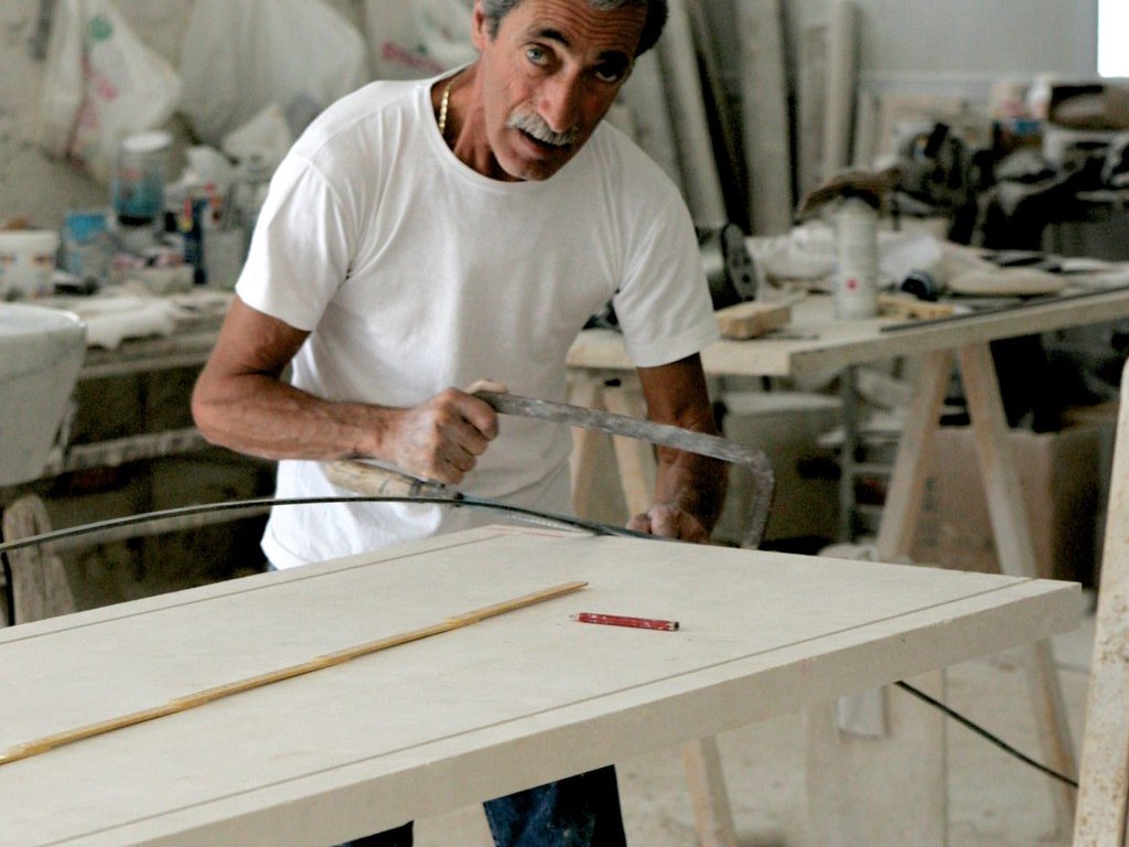 Craftsman in a workshop cutting a long wooden board with a hand saw