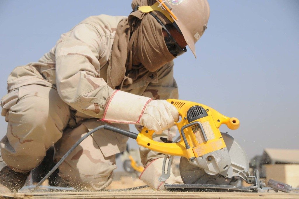 Tradesperson in a hard hat and safety glasses cutting wood with a circular saw